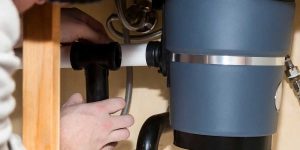 Hands adjust plumbing pipes under a kitchen sink to disconnect a garbage disposal and install a standard drain line.